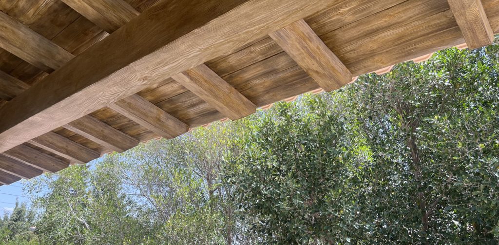 Detalle de vigas y tableros de hormigón imitación madera en un porche rústico en Alicante